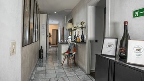 A hallway with a tiled floor, framed pictures on the walls, a desk with a lamp, and a chair. There is a framed certificate on a cabinet. - Gate 40 (Rome)