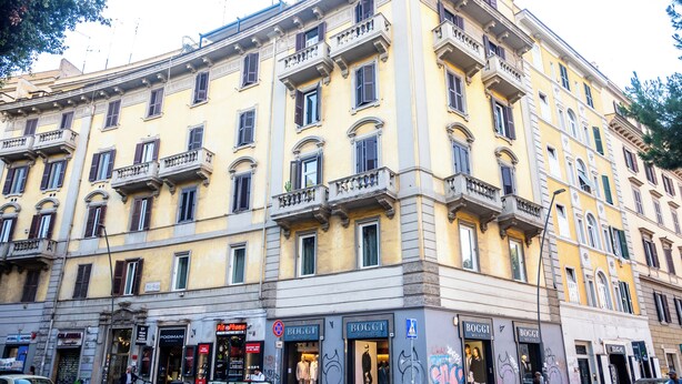A multi-story building with storefronts on the ground floor, including a clothing store named 'BOGGI'. - Gate 40 (Rome)