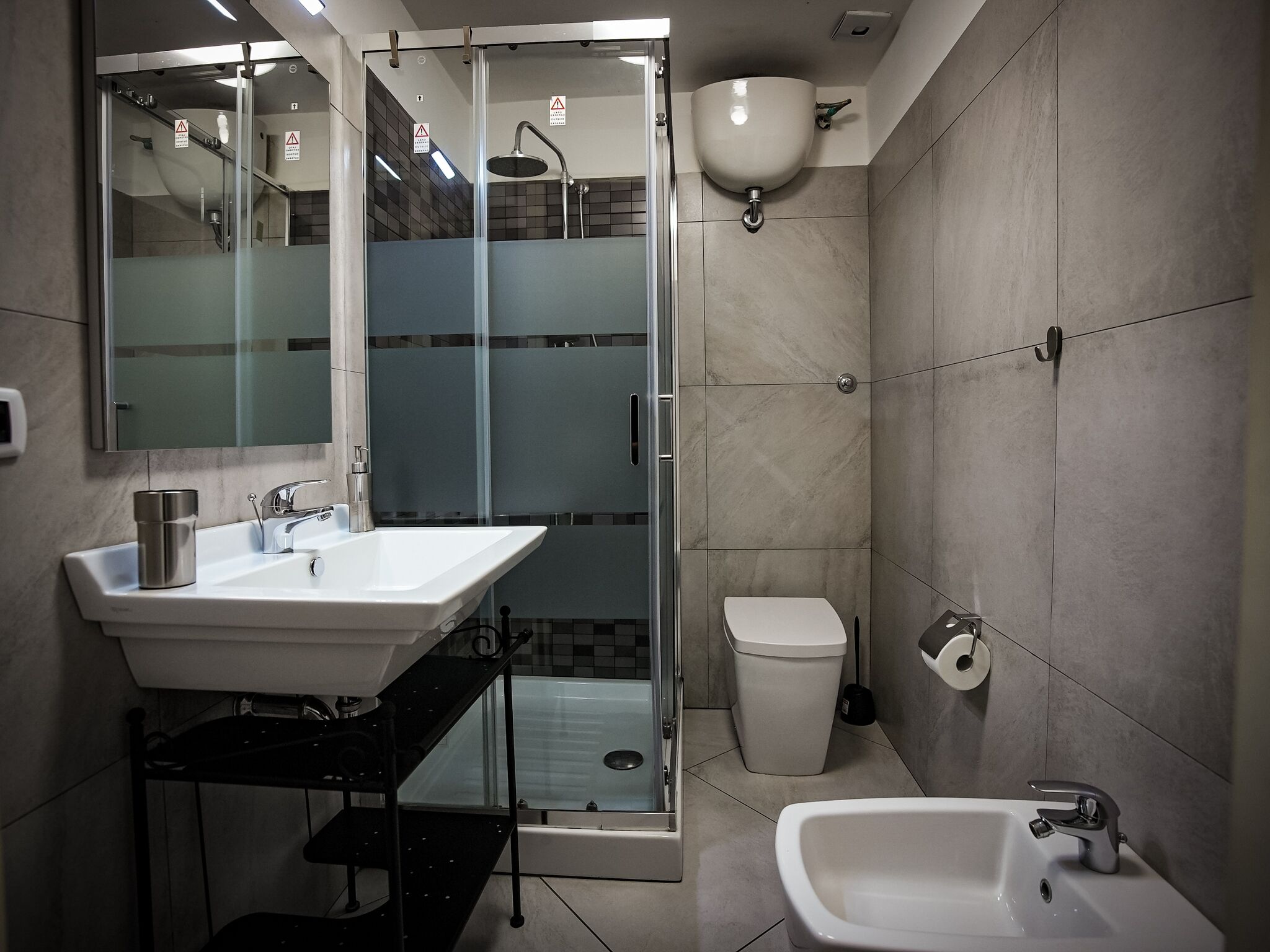 Un baño moderno con ducha de mampara de vidrio, un lavamanos blanco y un bidé.
