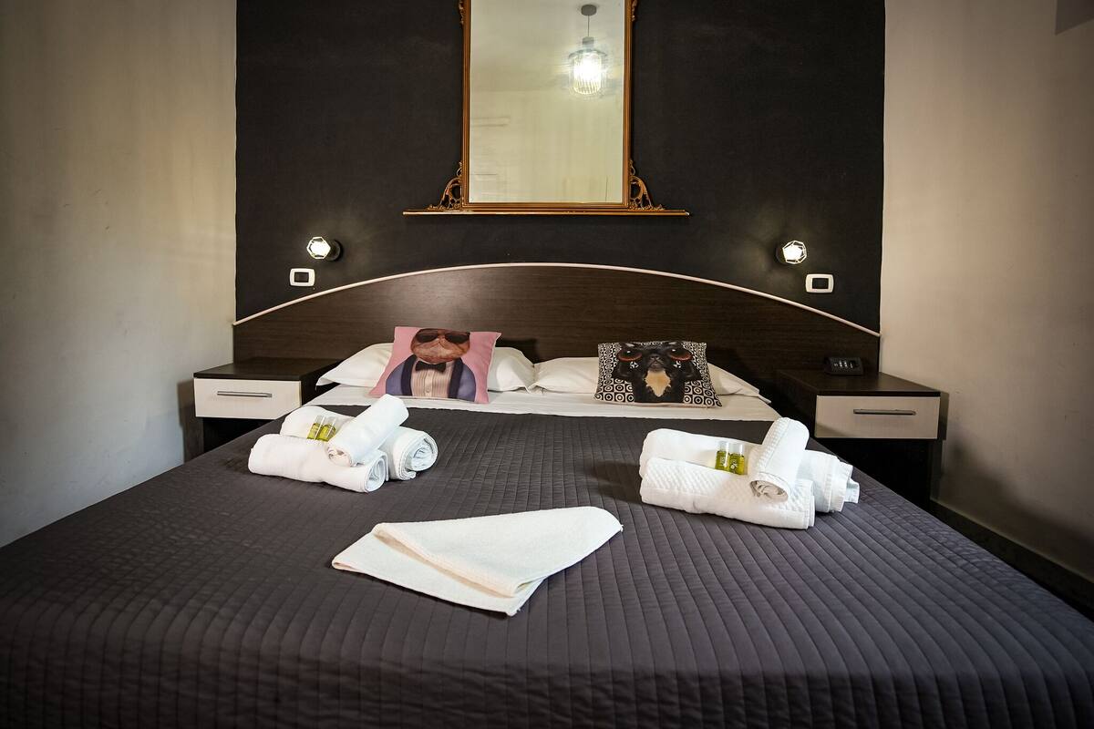A neatly made bed with towels, a headboard mirror, and bedside lamps.