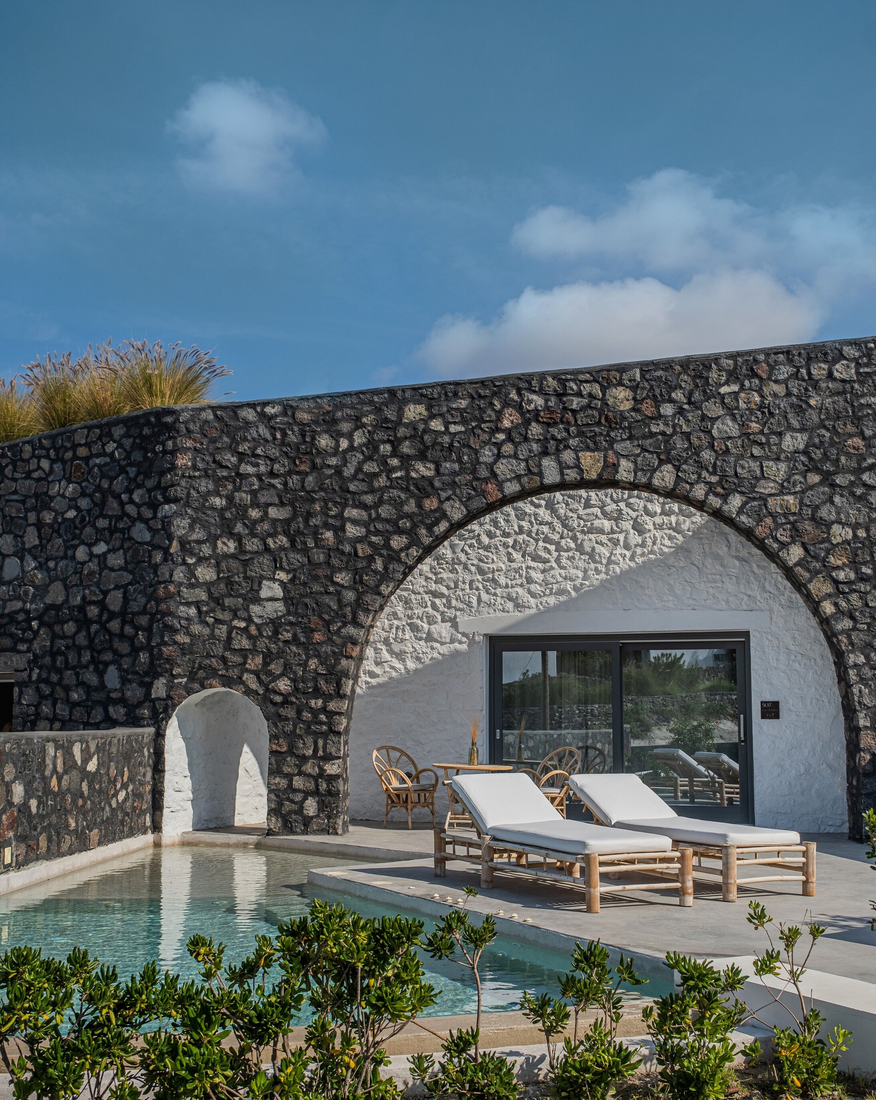 Zona de piscina con paredes de piedra, sillas de descanso y entrada de vidrio.