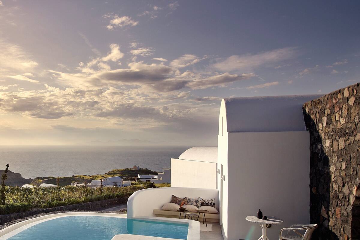 Ein modernes Außenpool-Areal mit einem weißen Infinity-Pool, einer Steinmauer und einem Gebäude mit gewundener Dachlinie.