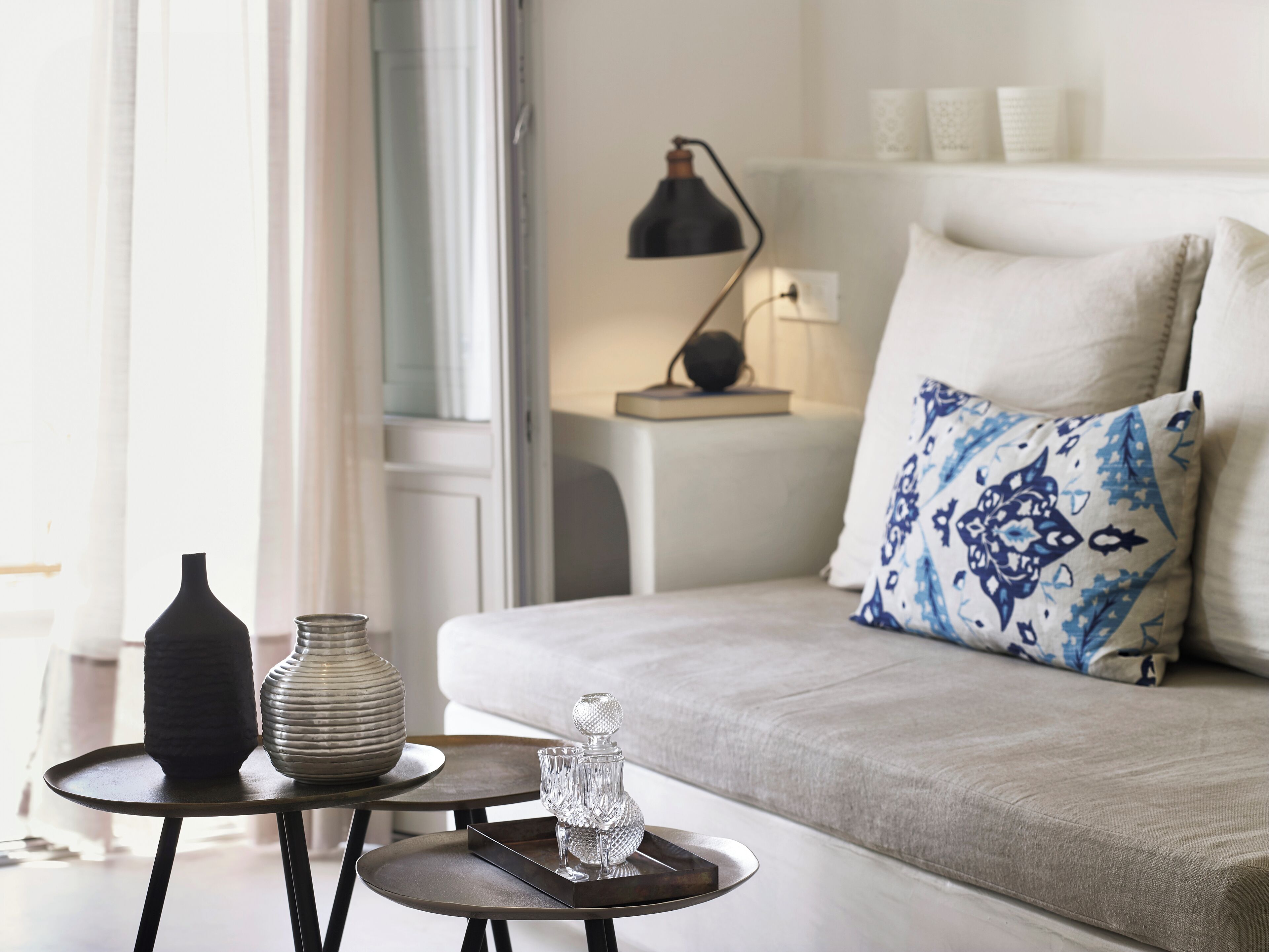 A modern living room with a grey sofa, a patterned pillow, a small round table with decorative items, and a floor lamp.