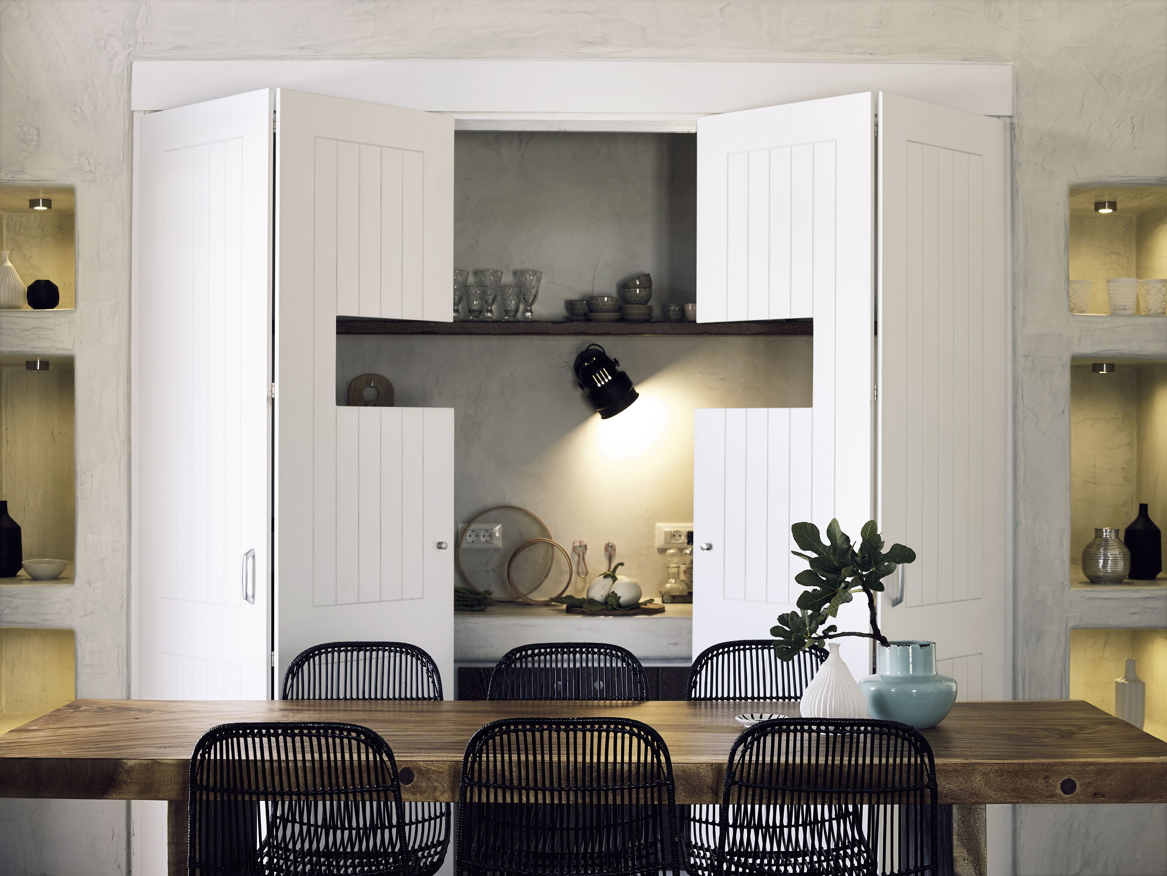 A dining area with a wooden table and black wire chairs, a white cabinet with shelves above, and a black pendant light.