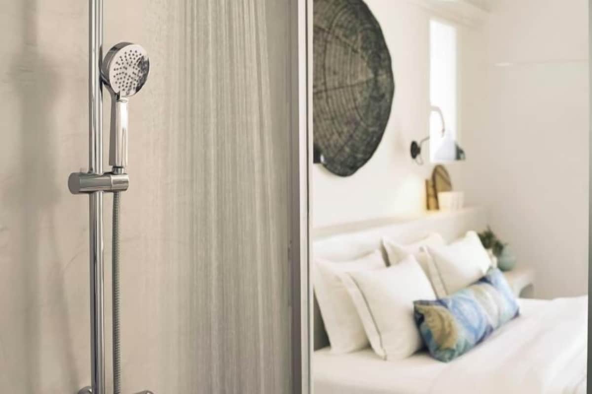 A bathroom with a shower, a bed with pillows, and a wall-mounted light fixture.