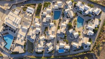 An aerial view of a resort with multiple bungalow-style accommodations, a central swimming pool, and landscaped areas.