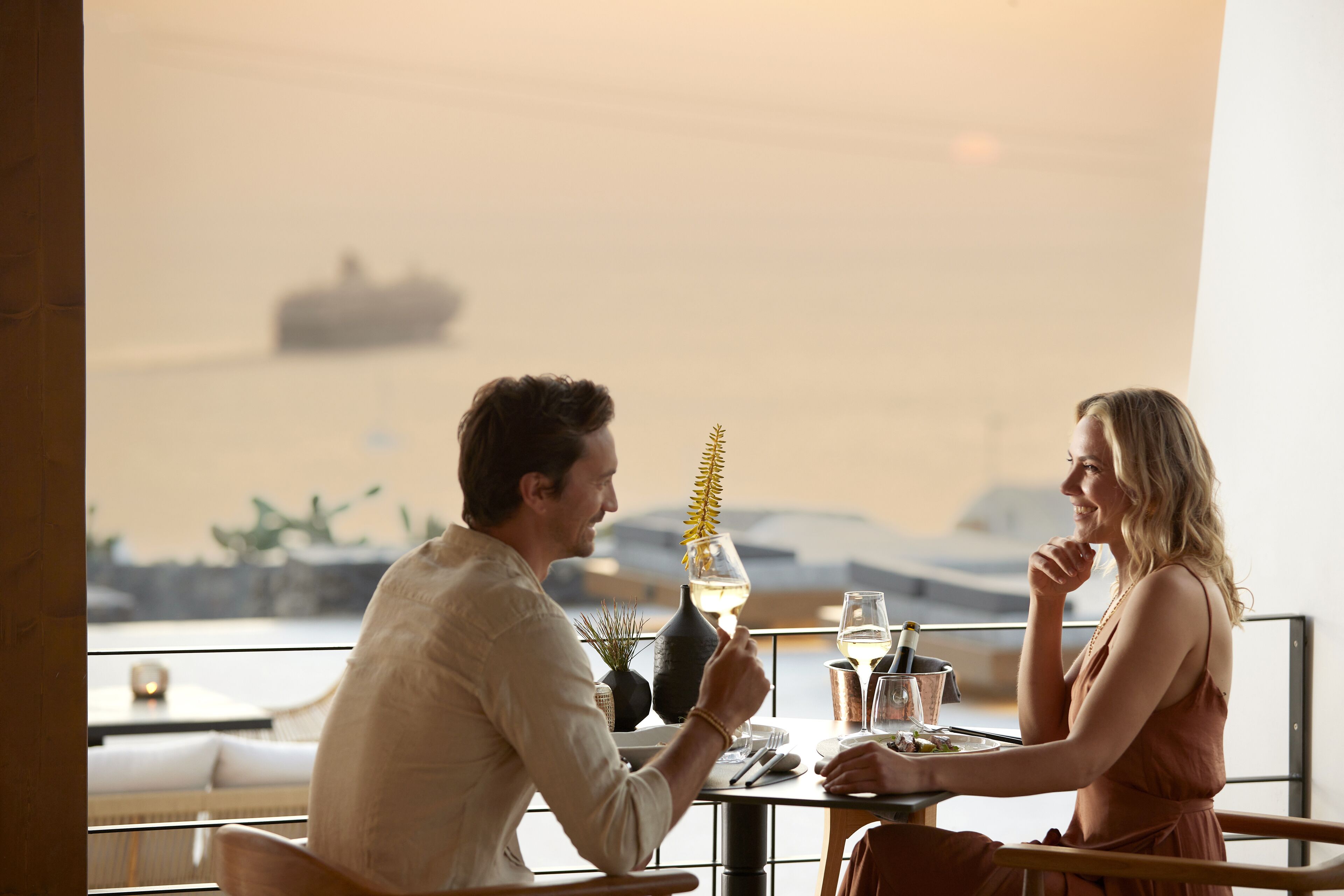 Ein Paar speist an einem Tisch mit Blick auf das Meer und ein Schiff in der Ferne.