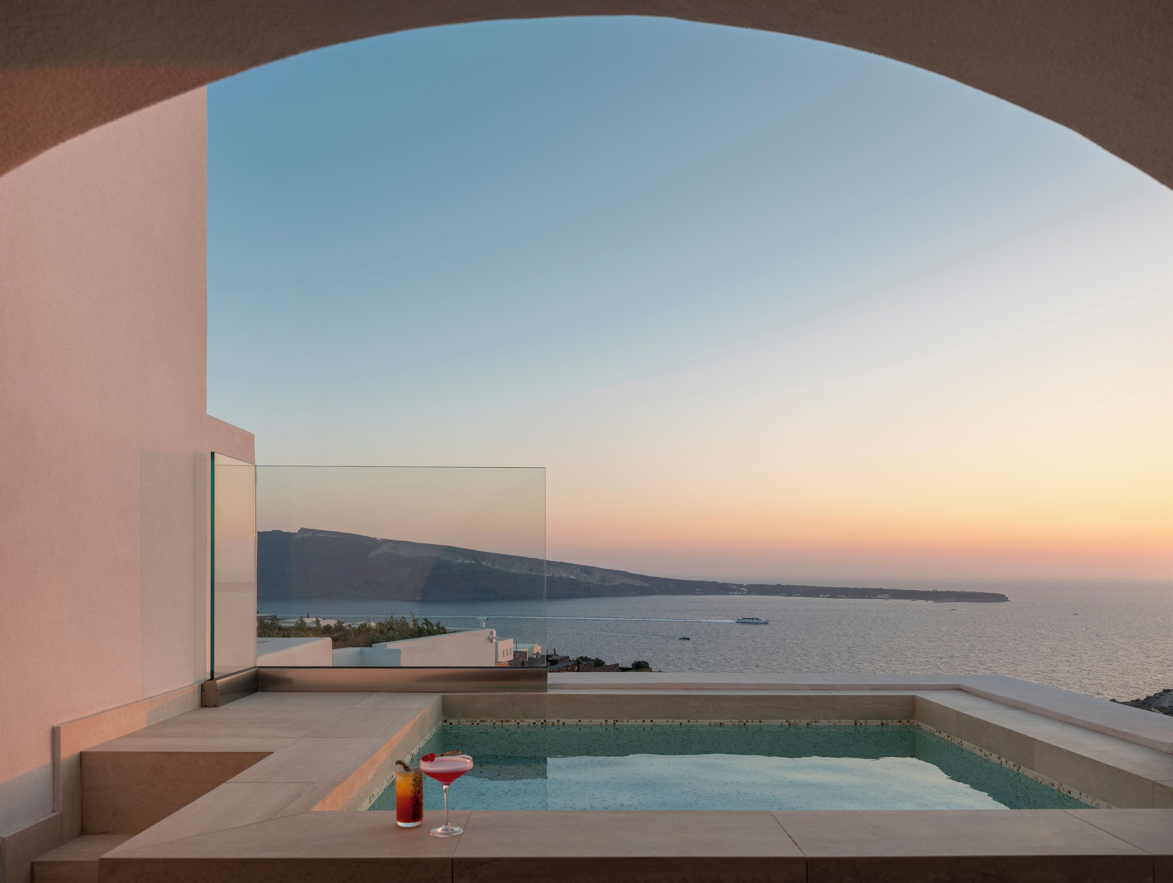 A modern infinity pool with a clear view of the sea and distant land during sunset.