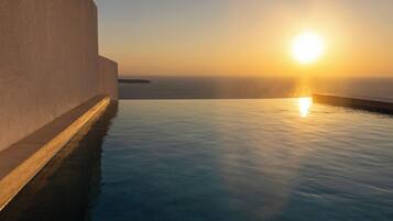 A serene infinity pool with a sunset view, a smooth white wall, and calm water reflecting the sky.