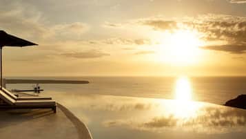 A serene infinity pool with a lounge chair and umbrella, overlooking a calm sea and a sunset.