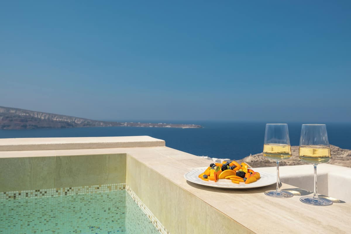 Blick auf einen Pool mit blauem Himmel, einem Obstteller und zwei Weingläsern.
