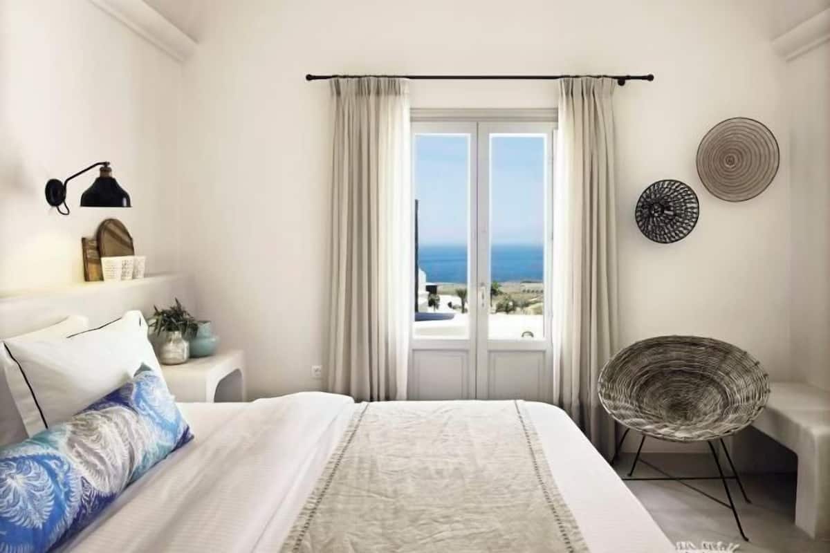 Ein Schlafzimmer mit Bett, Stuhl, Fenster mit Vorhängen, Lampe und Wanddekoration.