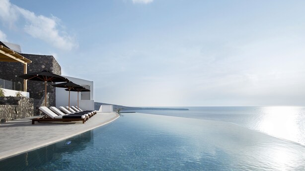 Zona junto a la piscina con sillas de descanso y sombrillas, con vista a un mar azul y transparente.