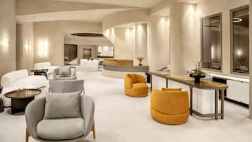 A spacious, modern living area with a curved reception desk, comfortable seating, and a large mirror reflecting the interior.