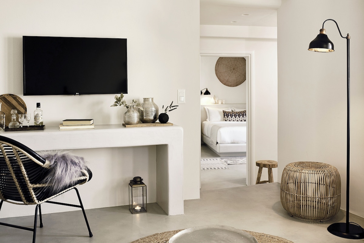 Una sala de estar moderna con una consola blanca, un sillón de cuero negro, un taburete redondo tejido y una lámpara de pie negra.
