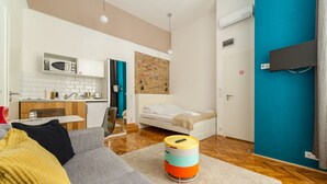 A modern apartment with a kitchenette, a sofa, a bed, and a colorful ottoman. - Tatra 4 Studios (Budapest)