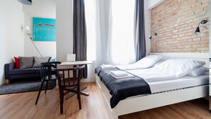 A modern bedroom with a brick wall, a desk, a bed, and a view of the cityscape. - Tatra 4 Studios (Budapest)