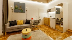 A modern living room with a grey sofa, a small round coffee table, and a kitchen area with wooden cabinets and a white countertop. - Tatra 4 Studios (Budapest)