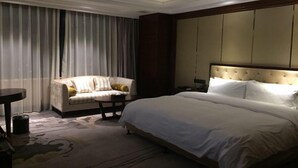A hotel room with a large bed, a sofa, a small table, and a nightstand. - Jialaite Garden International Hotel (Nanchang)