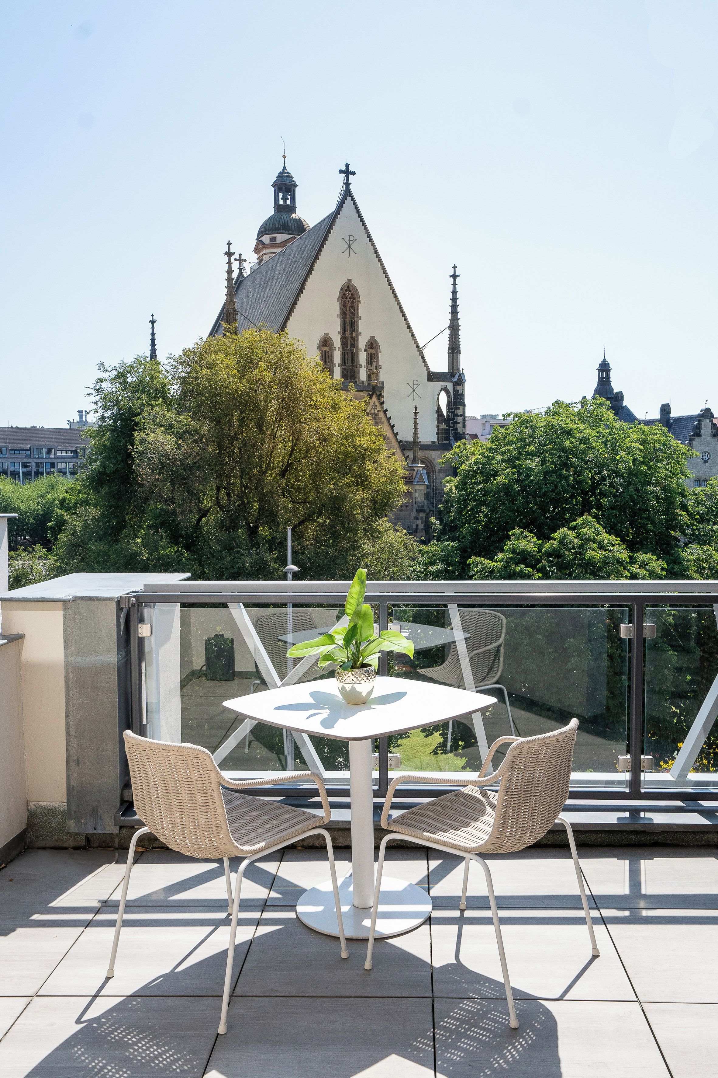 Eine Dachterrasse mit Tisch und Stühlen, mit Blick auf eine historische Kirche mit einem Glockenturm.