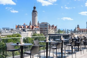 A rooftop terrace with tables and chairs, overlooking a historic cityscape with a prominent tower. - INNSiDE by Meliá Leipzig (Leipzig)