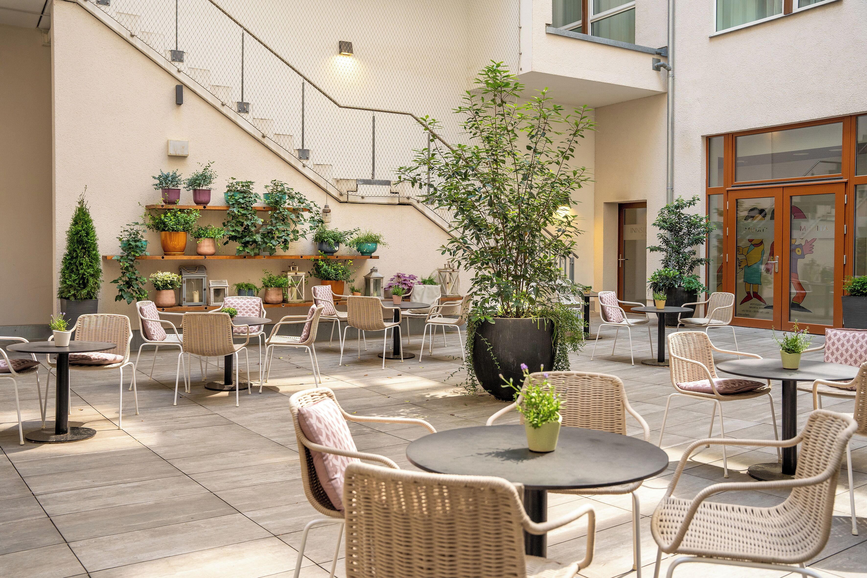 Un patio al aire libre con mobiliario de mimbre, plantas en macetas y una escalera que conduce a un nivel superior.