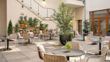 Un patio al aire libre con mobiliario de mimbre, plantas en macetas y una escalera que conduce a un nivel superior.