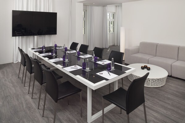 Une salle de conférence moderne, dotée d’une longue table, de chaises noires et d’un mur d’accent blanc.