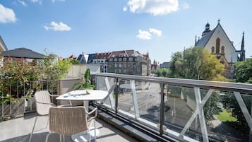 A balcony with wicker chairs and a table, overlooking a cityscape with historic buildings and a church.