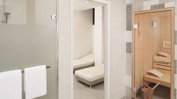Un baño moderno con cabina de ducha de vidrio, un banco de madera y un pequeño cubo de madera.