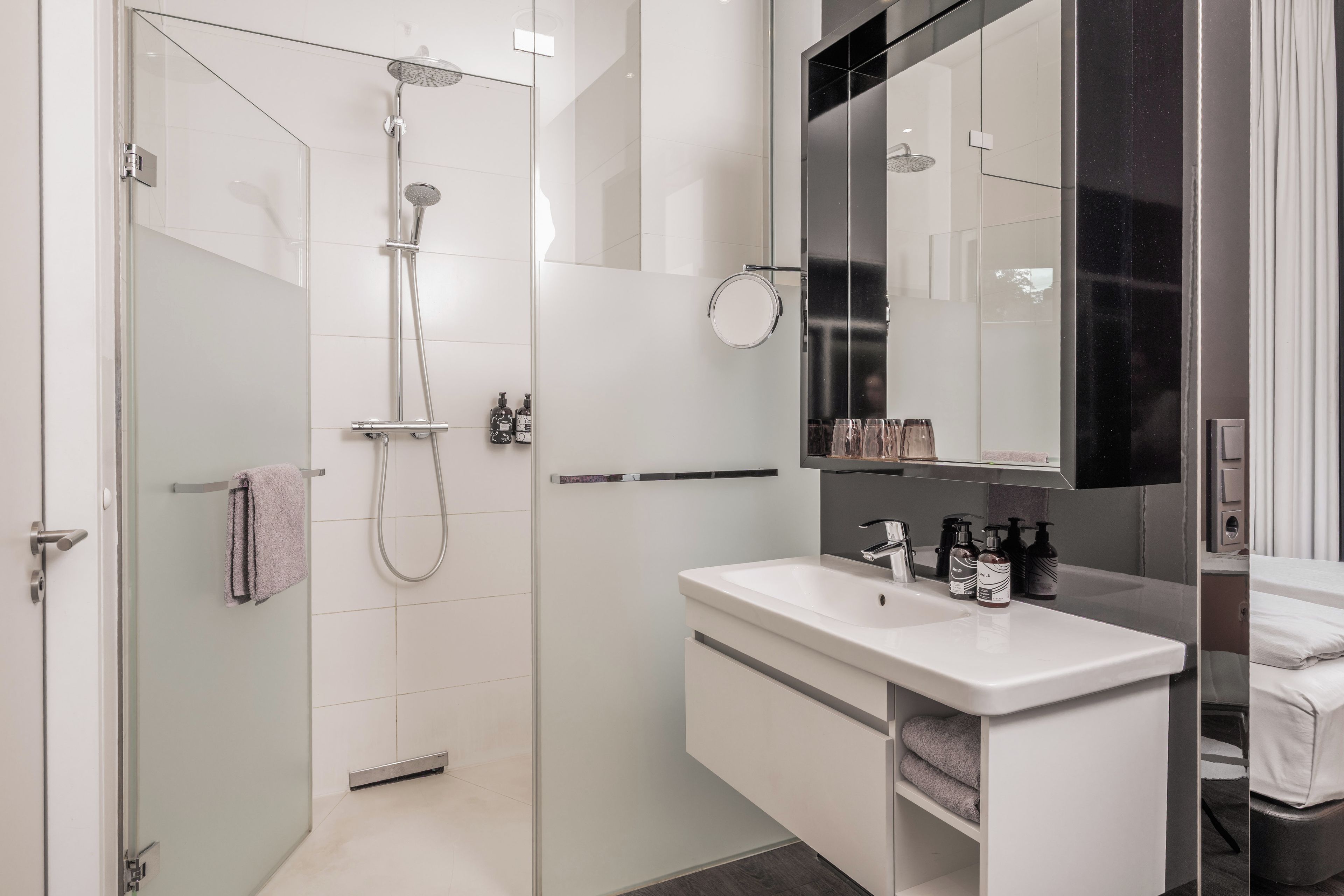 Un baño moderno con ducha envuelta en vidrio, un tocador blanco con espejo y un perchero.
