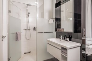 Un baño moderno con ducha envuelta en vidrio, un tocador blanco con espejo y un perchero.