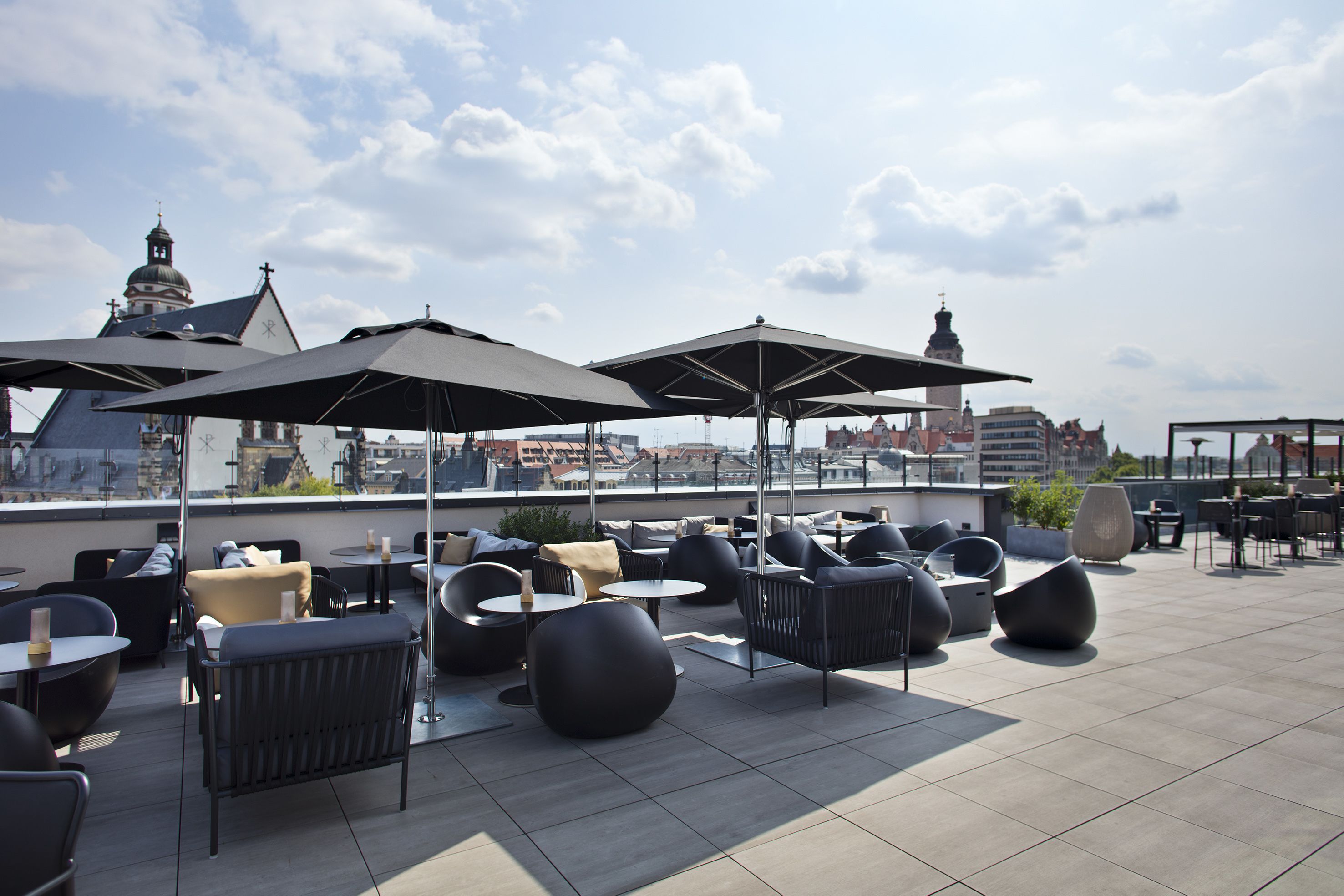 Eine Dachterrasse mit Sitzgelegenheiten im Freien, Sonnenschirmen und Blick auf die Stadtlandschaft.