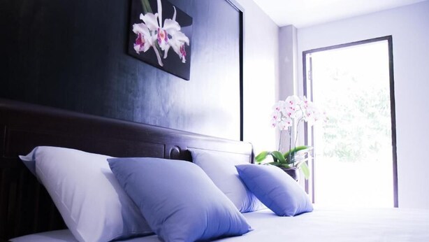 Een slaapkamer met een groot bed, twee kussens, een donker hoofdeinde, een raam met uitzicht en een potplant.