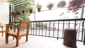 Een balkon met houten stoelen en een tafel, planten in potten, en uitzicht op de straat.