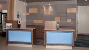 A reception area with two reception desks, a wall-mounted security camera, and a sign indicating check-in and check-out times.