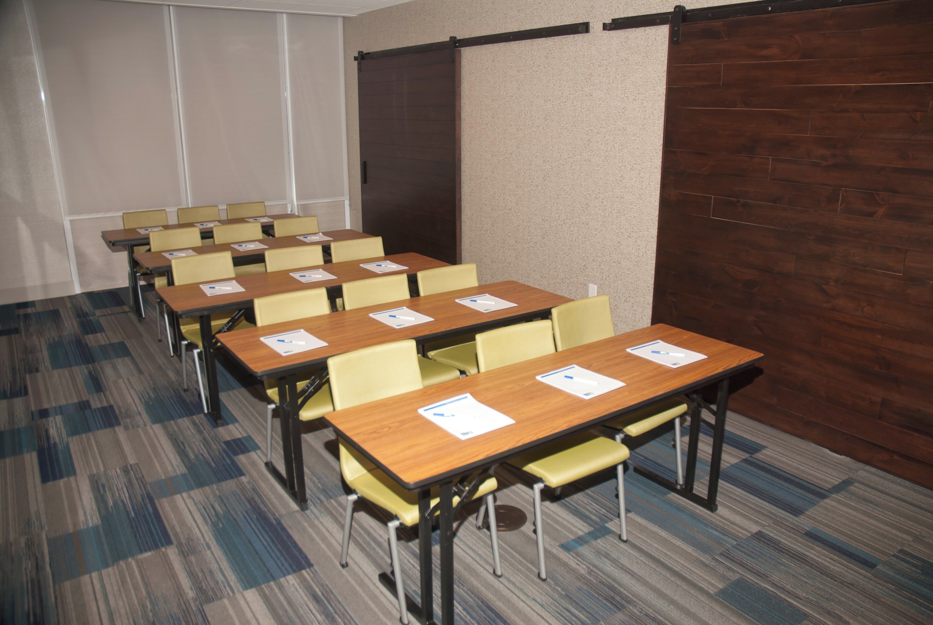 A conference room with rows of tables and chairs, a carpeted floor, and a wooden partition wall.