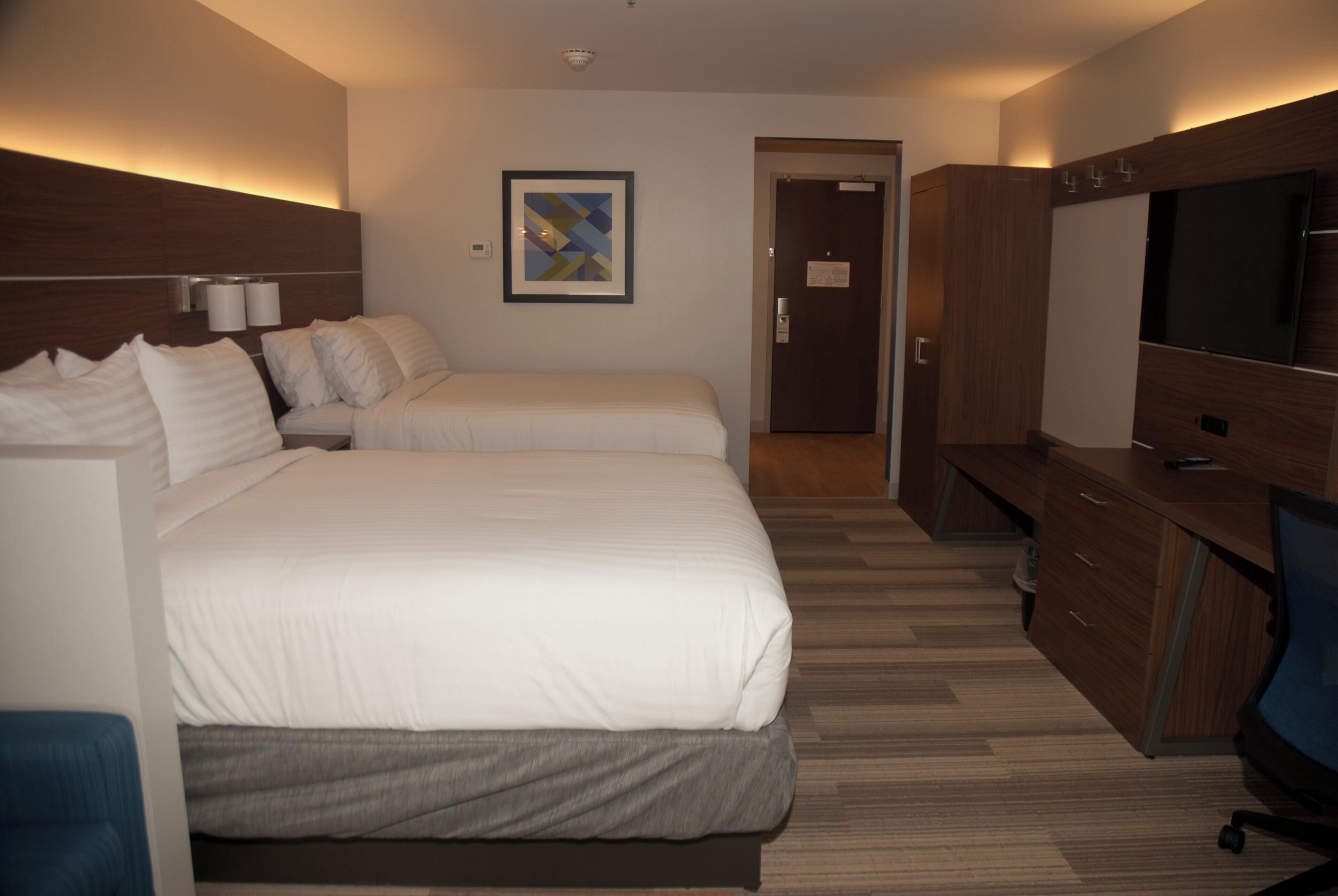 Une chambre d’hôtel avec deux lits, une télévision, un bureau et une porte donnant sur une autre chambre.