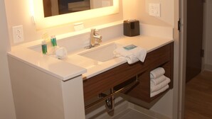 A modern bathroom with a white sink, a mirror with integrated lighting, a towel rack, and a wooden vanity. - Holiday Inn Express & Suites Decatur by IHG (Decatur)