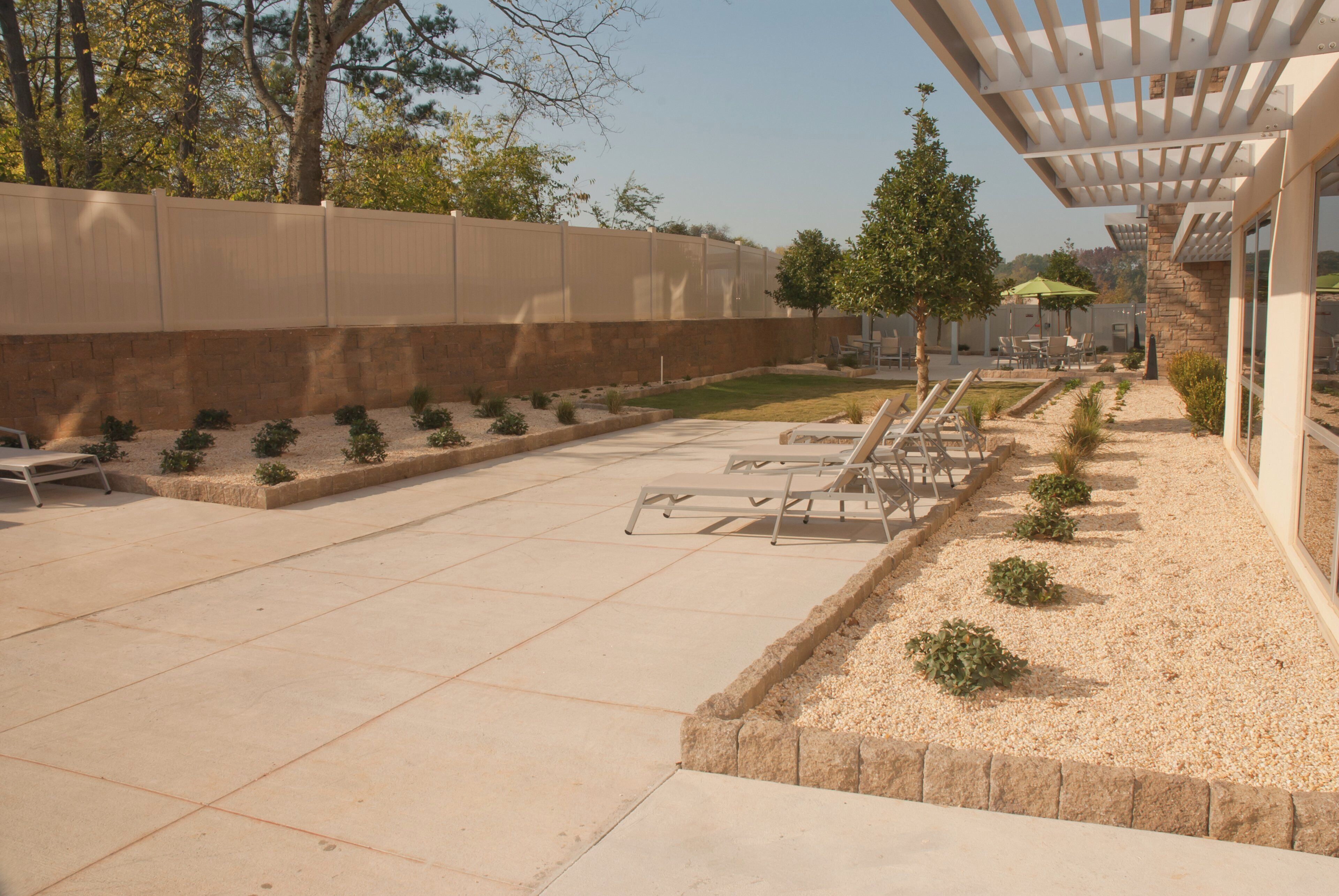 Un área de patio exterior con un pérgola, asientos y un pequeño jardín.