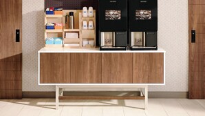 A wooden counter with two coffee machines, a shelf with coffee cups, and storage boxes. - Holiday Inn Express & Suites Decatur by IHG (Decatur)