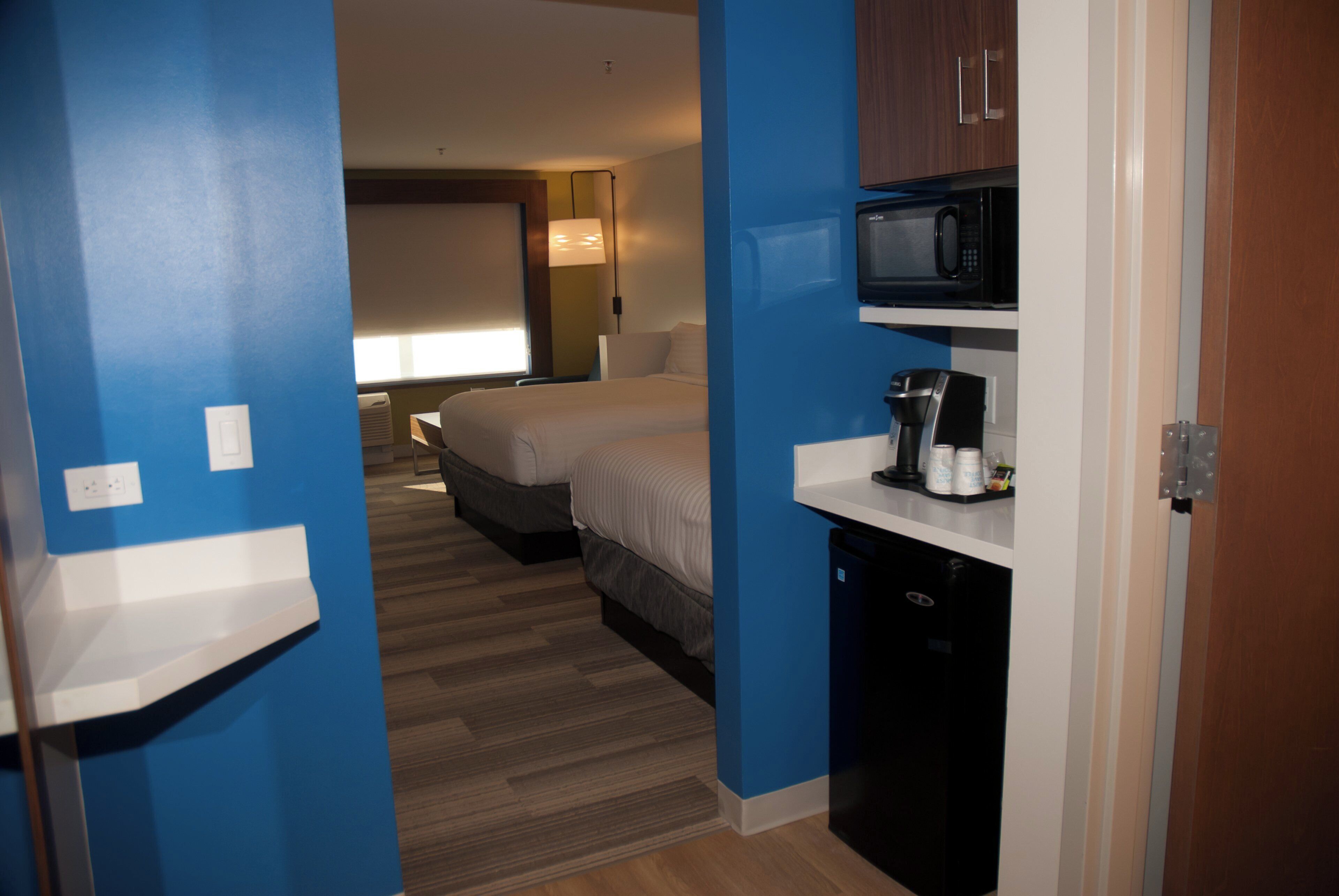 A hotel room with a bed, a microwave, a coffee maker, and a small kitchenette.