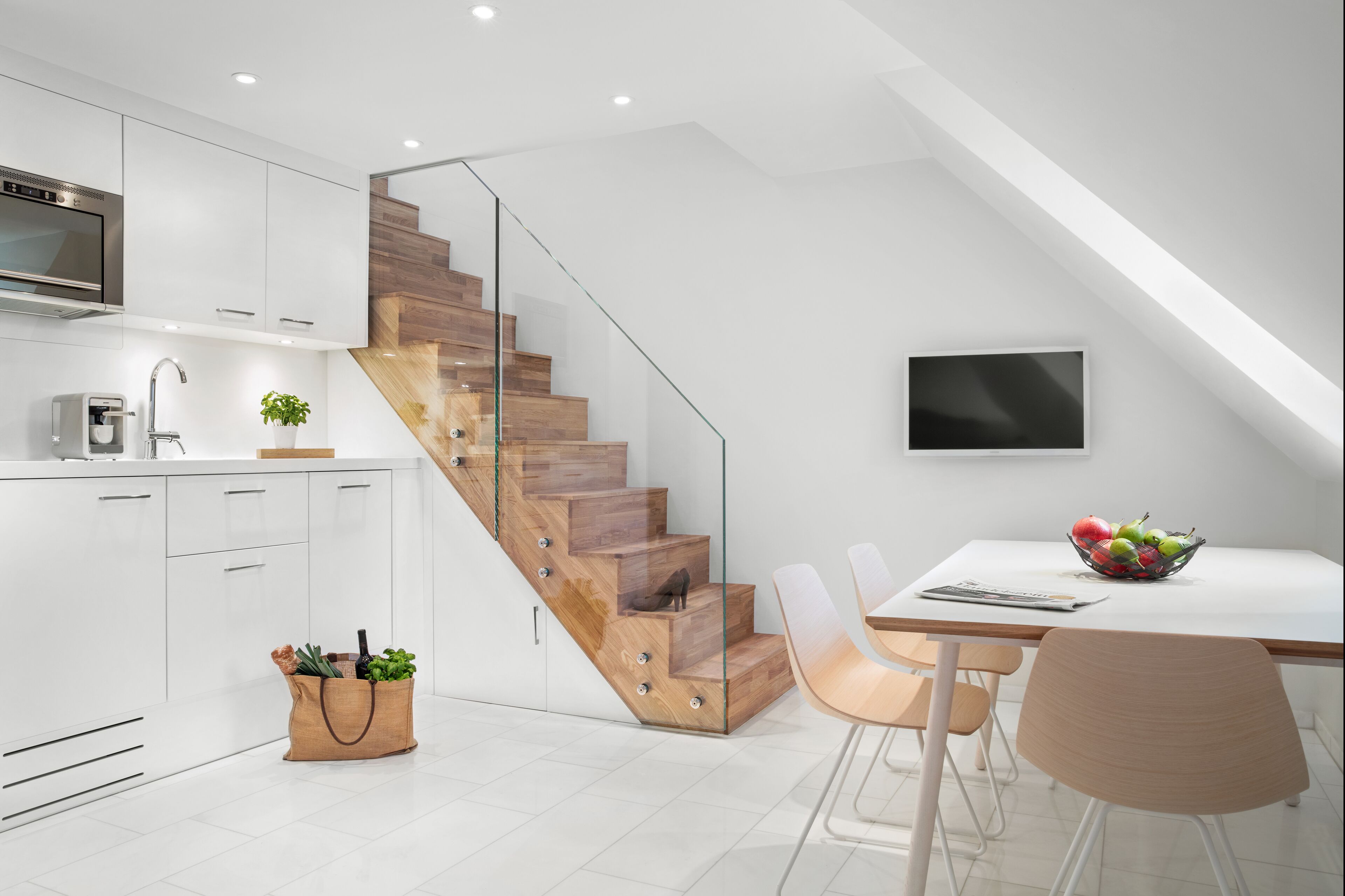 A modern kitchen with white cabinets, a wooden staircase, and a dining area with a table and chairs.
