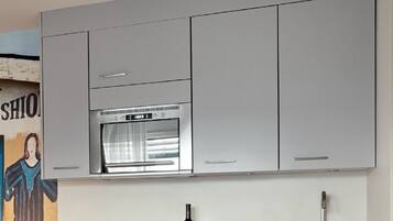 A modern kitchen with grey cabinets, a stainless steel oven, and a marble countertop.