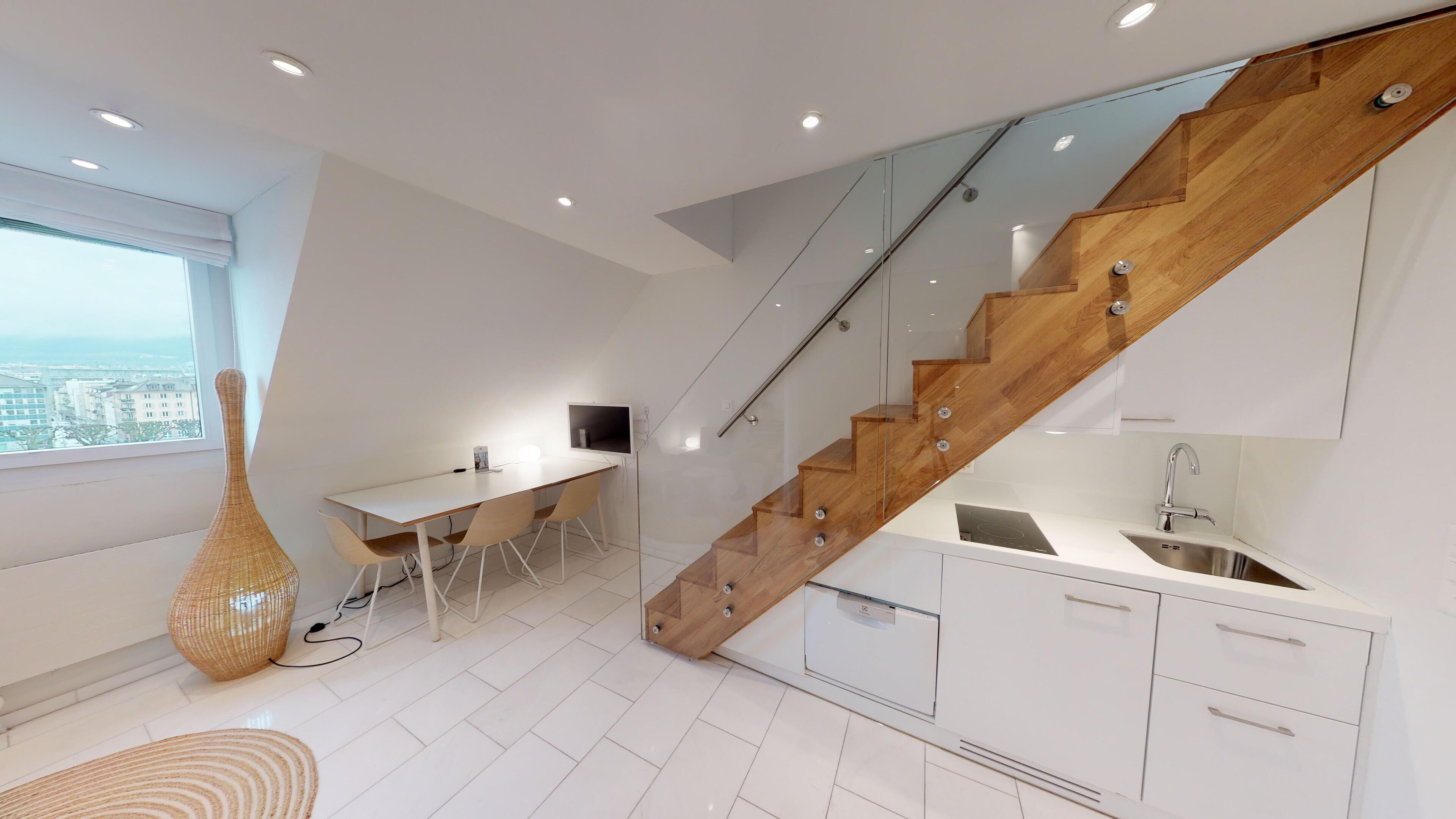 Eine moderne Küche mit einer Holztreppe, einem Essbereich mit weißem Tisch und Stühlen sowie einem großen Fenster mit Aussicht.