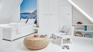 A modern bedroom with a white bed, a large window with a view of a coastal town, a white wardrobe, a reading chair, and a small bookshelf. - VISIONAPARTMENTS Zurich Militärstrasse (Zürich)