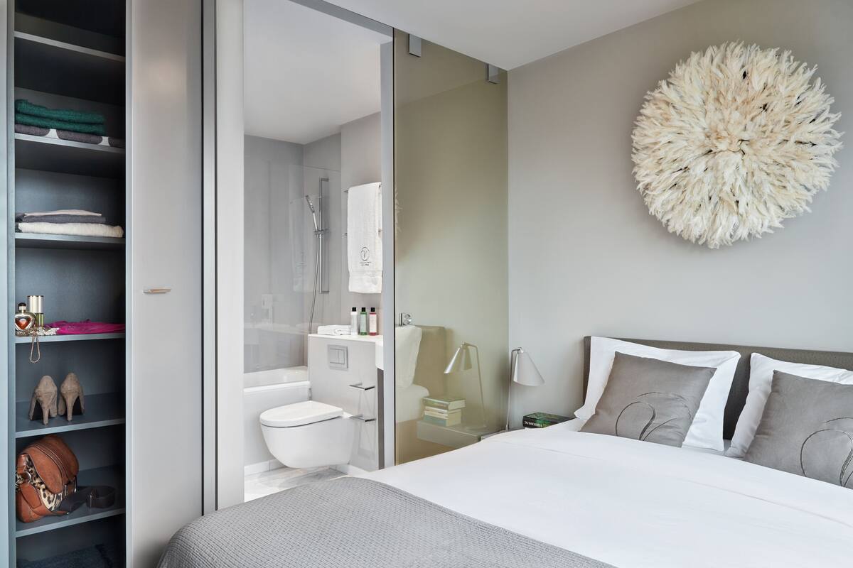 A modern bedroom with a large bed, a wardrobe, and a bathroom with a shower.