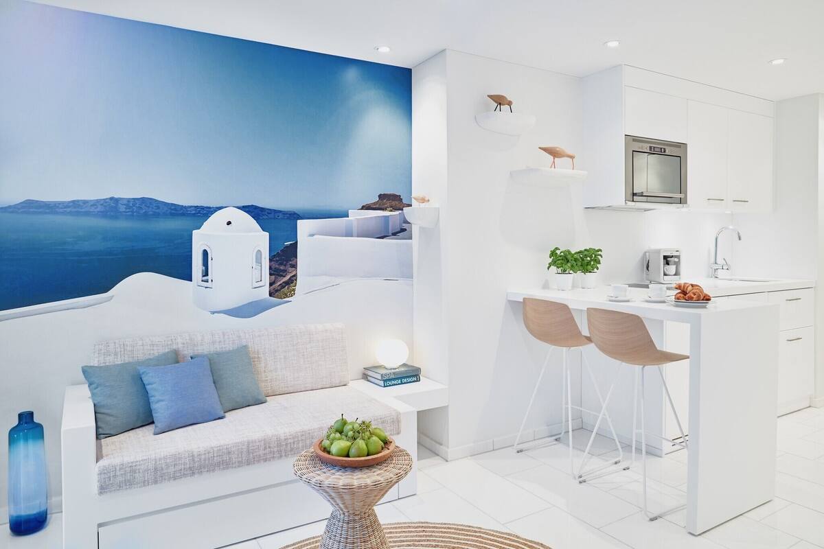 A modern kitchen with white cabinetry, a built-in oven, and a dining area with two chairs.