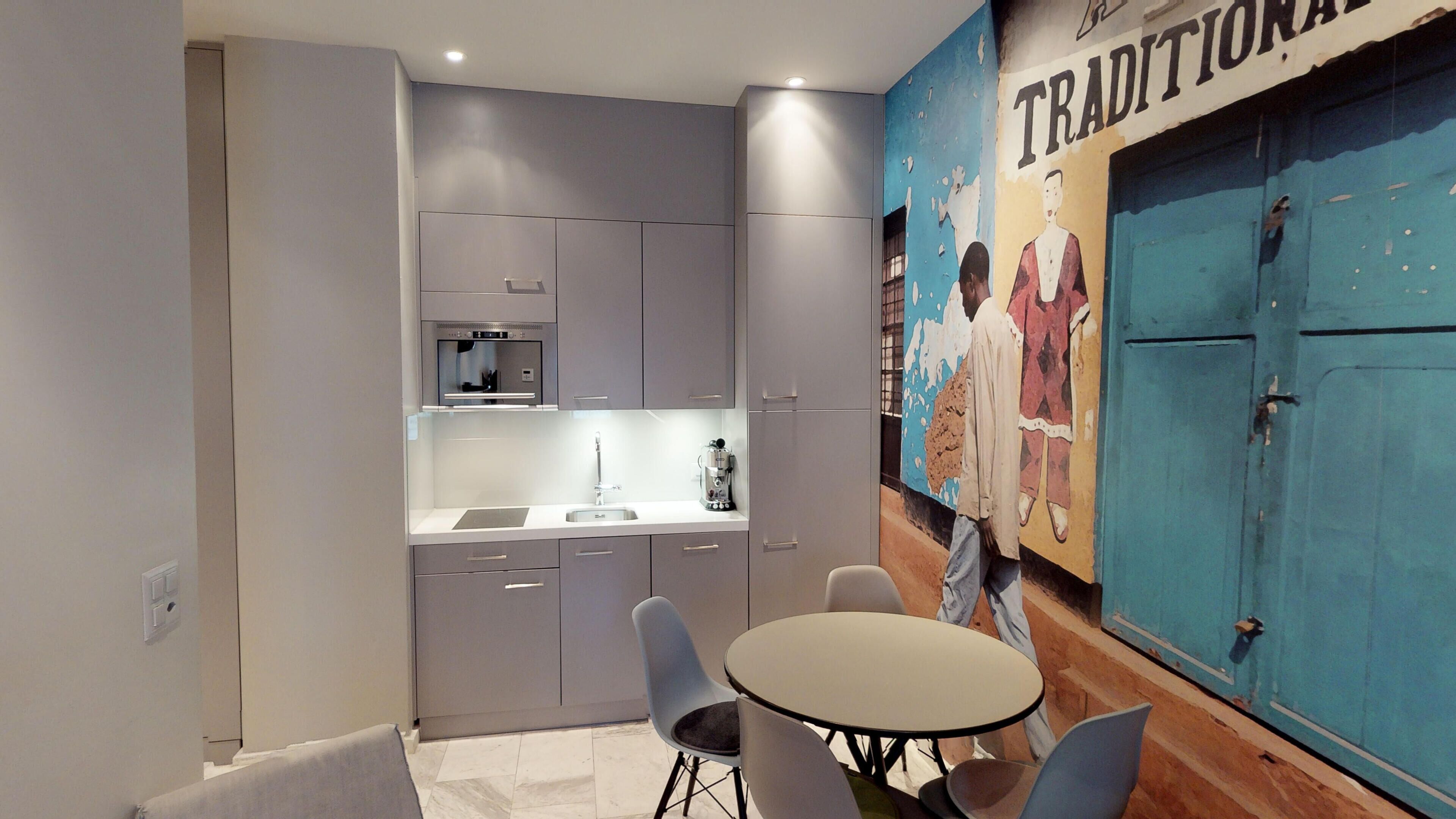 Una cocina compacta con electrodomésticos modernos, un comedor con una mesa redonda y sillas, y un mural en la pared.