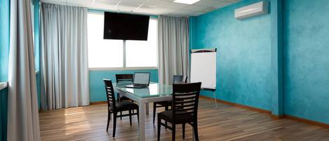 Un salón de conferencias con una mesa de vidrio, cuatro sillas, una computadora portátil, una pizarra y una televisión en la pared.